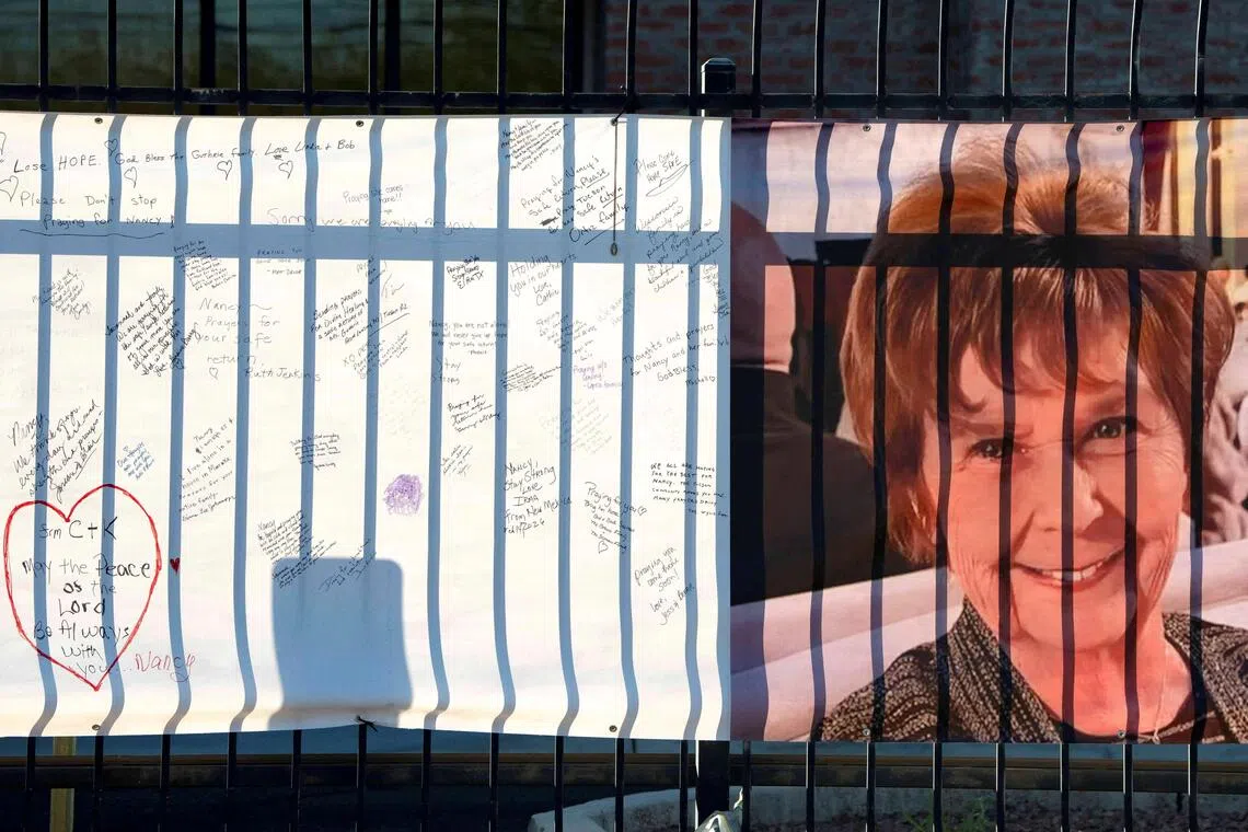 A memorial banner on a fence showing a woman's portrait and handwritten notes of support.