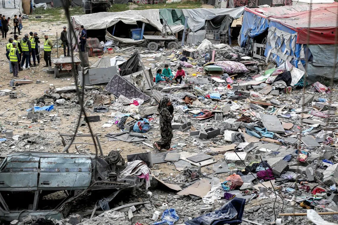 A woman carries a child as she walks through debris and rubble outside the Sabah family building that was hit by Israeli air strikes in Deir el-Balah in the central Gaza Strip on April 8.