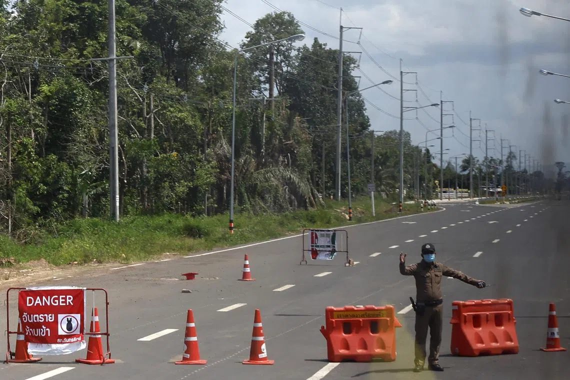 A Thai police officer standing guard next to an explosive danger sign on a main road in Kantharalak District, Sisaket Province, Thailand, Aug 1, 2025. 