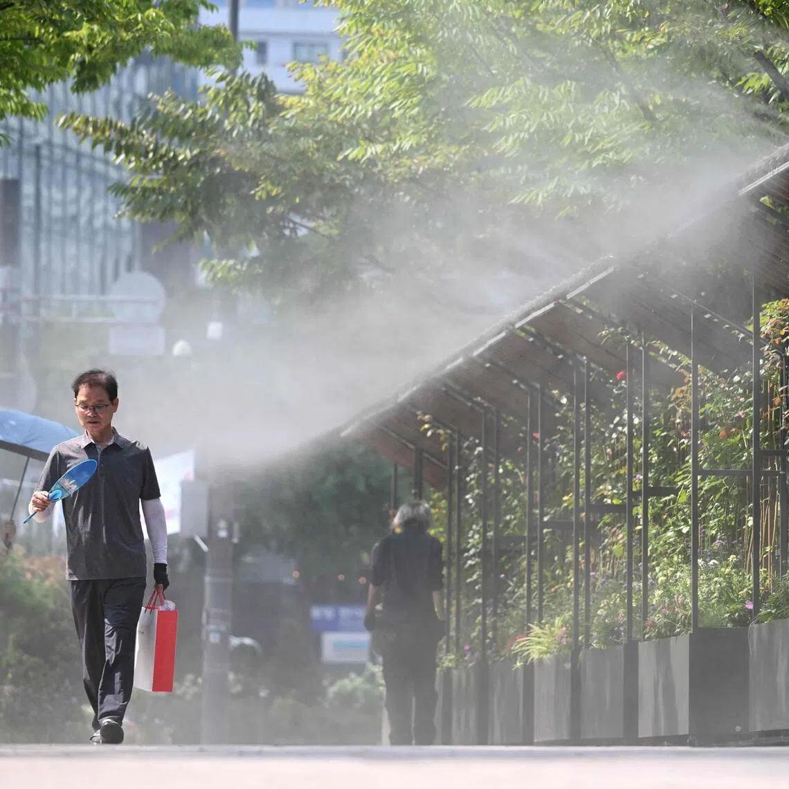 TOPSHOT - Pedestrians walk along a mist-spraying zone to cool off on a street in Seoul on August 3, 2026, as a scorching heat wave continues to grip South Korea. South Korea registered its highest temperature since records began more than a century ago on August 2, as authorities warned people to "immediately" stop all outdoor activities in affected areas. (Photo by Jung Yeon-je / AFP)