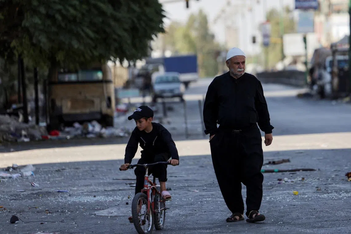 A man walks on a street, next to a child riding a bicycle, following deadly clashes between Druze fighters, Sunni Bedouin tribes and government forces, in Syria's predominantly Druze city of Sweida, Syria July 25, 2025. REUTERS/Khalil Ashawi/File Photo