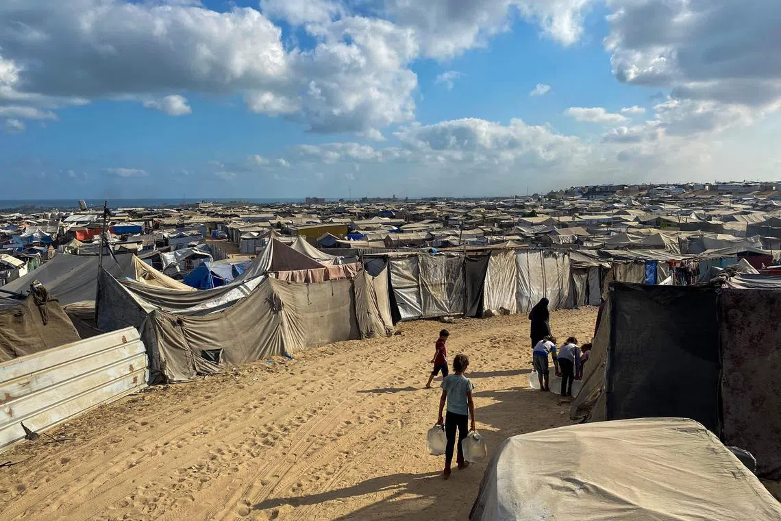 Palestinian children carrying water jugs on Aug 7 past tents housing displaced people in the southern Gaza Strip.