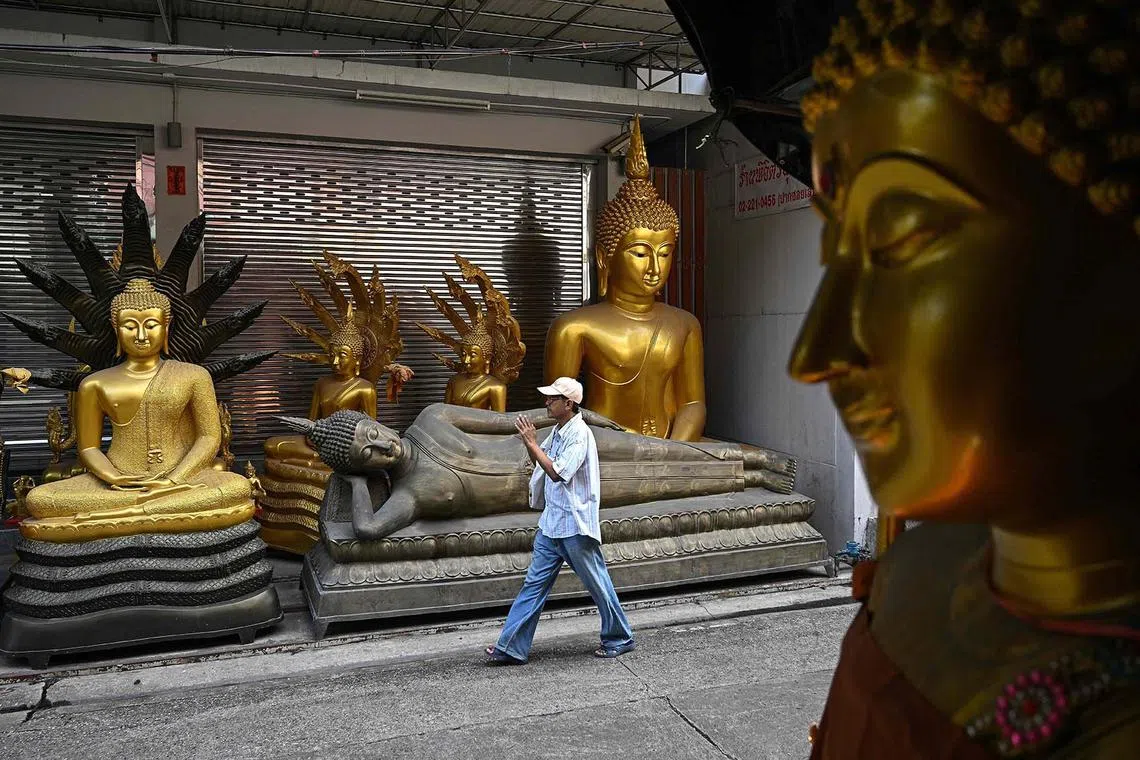 TOPSHOT - A man pays his respect with folded hands as he walks past Buddha statues kept for sale at a Buddhist religious supplies shop in Bangkok on October 16, 2024. (Photo by Manan VATSYAYANA / AFP)