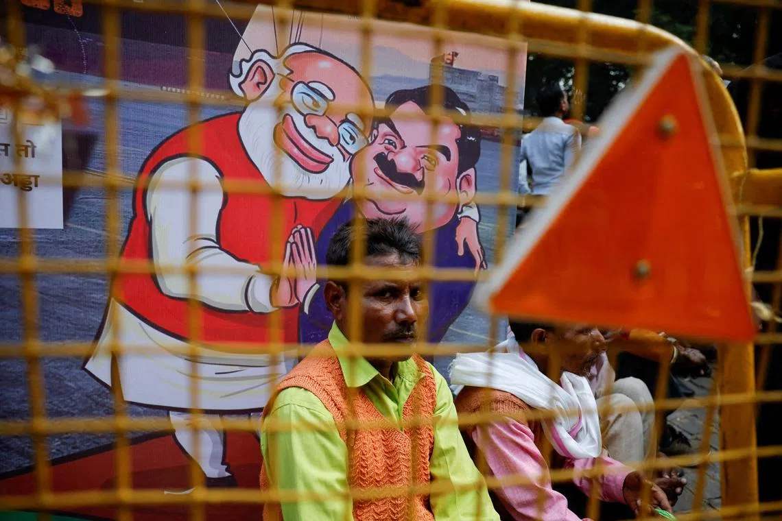 FILE PHOTO: A man sits next to a poster put up during a protest by India's main opposition Congress party against Indian billionaire Gautam Adani, after he was indicted in New York over his role in an alleged multibillion-dollar bribery and fraud scheme, in New Delhi, India, November 25, 2024. REUTERS/Anushree Fadnavis/File Photo