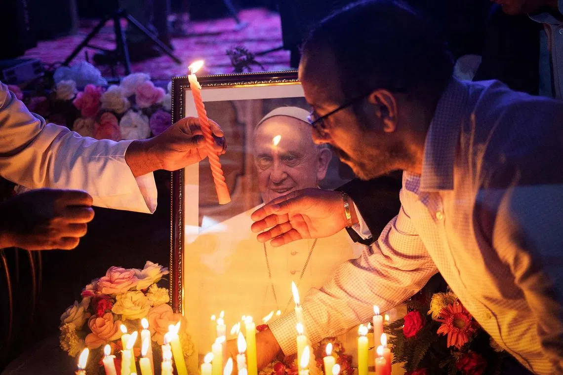 People lighting candles in front of a picture of Pope Francis, after his death was announced by the Vatican, during a condolence meeting in New Delhi, India, April 21, 2025. 