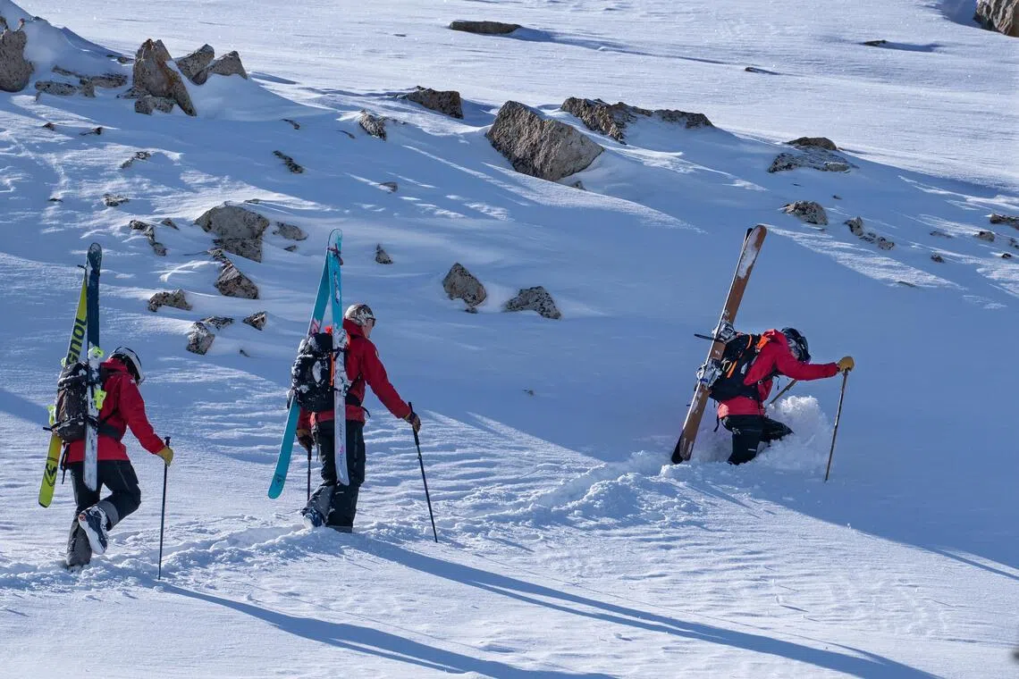 Ski patrollers hike towards a high ridge to determine if the area can be safely opened to skiers for the next day, at Snowbird, a ski resort near Alta, Utah.