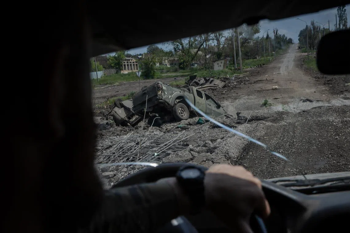 A member of Ukraine's 93rd Mechanized Brigade drives past destroyed vehicles on a road outside Bakhmut, Ukraine.