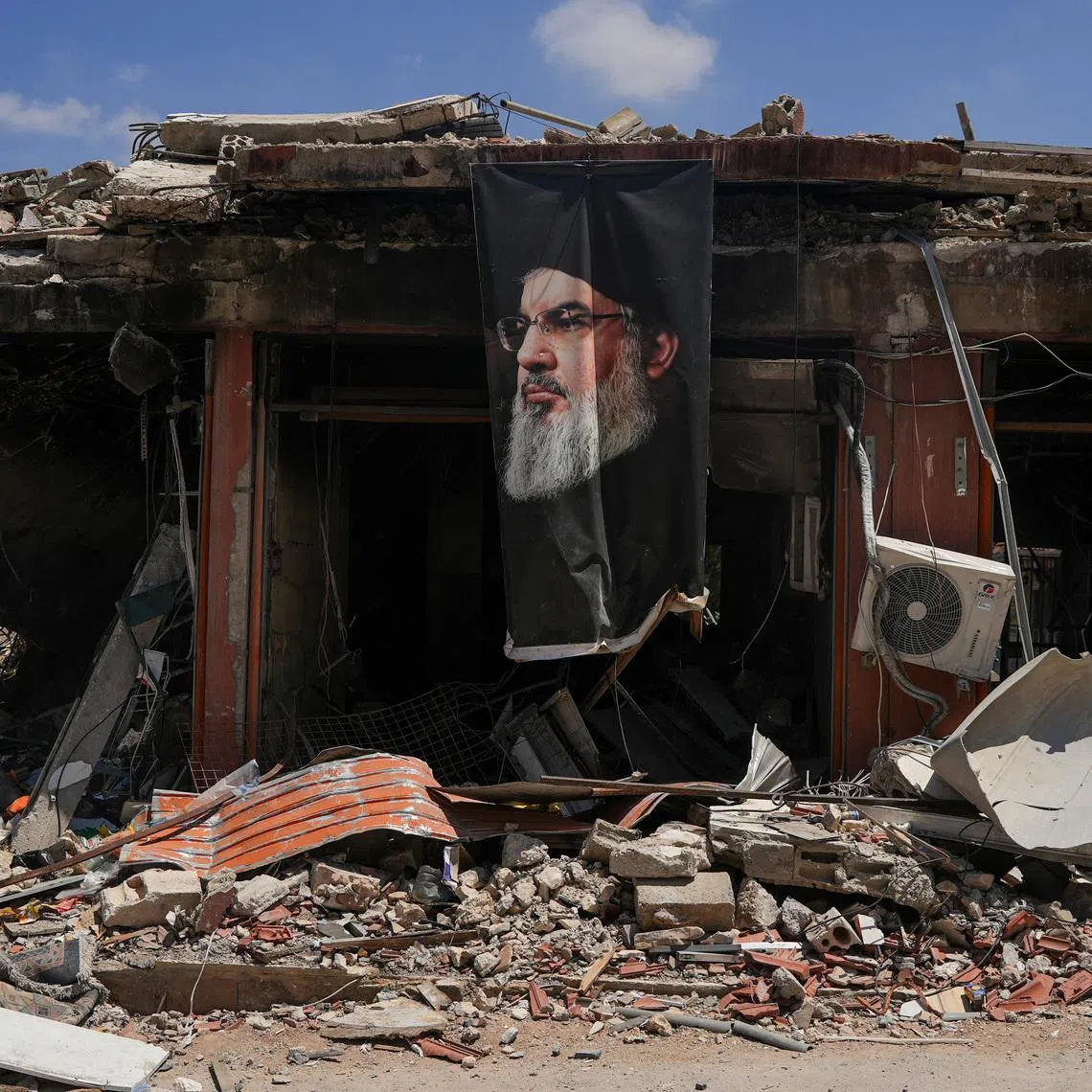 A banner with an image of late Hezbollah leader Hassan Nasrallah hangs from a destroyed building in Jibchit, Nabatieh district, Lebanon, June 16, 2026, following a deal between the United States and Iran. REUTERS/Stringer