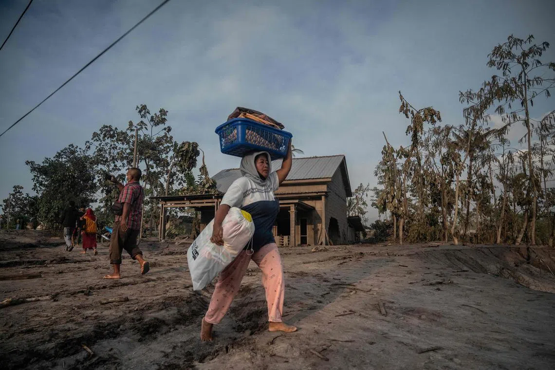 A woman salvages belongings following a volcanic eruption by Mount Semeru at Kajar Kuning village in Lumajang on Dec 5, 2022. 