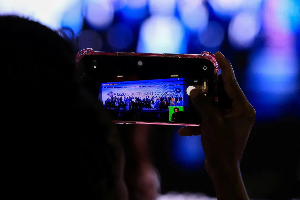 A person uses their phone to capture the leaders family photo on a big screen, on the opening day of the G20 leaders' Summit at the Nasrec Expo Centre in Johannesburg, South Africa, November 22, 2025. REUTERS/Esa Alexander/File Photo
