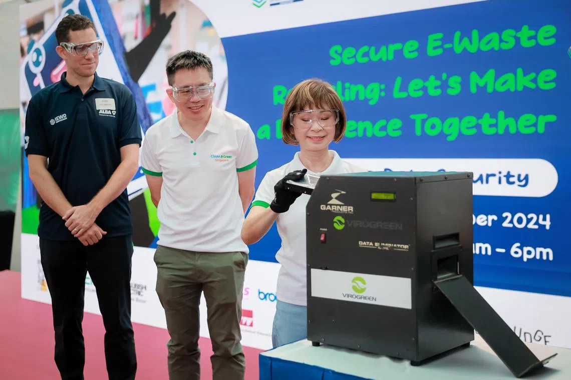 Senior Minister of State for Sustainability and the Environment Dr Amy Khor putting a used hard drive into a hard drive degausser during the launch of the International E-Waste Day (IEWD) celebration held at Westgate Mall on Oct 13, 2024. With her are ALBA E-Waste Chief Executive Officer Jakob Lambsdorff (left) and National Environment Agency Chief Executive Officer Wong Kang Jet (centre).