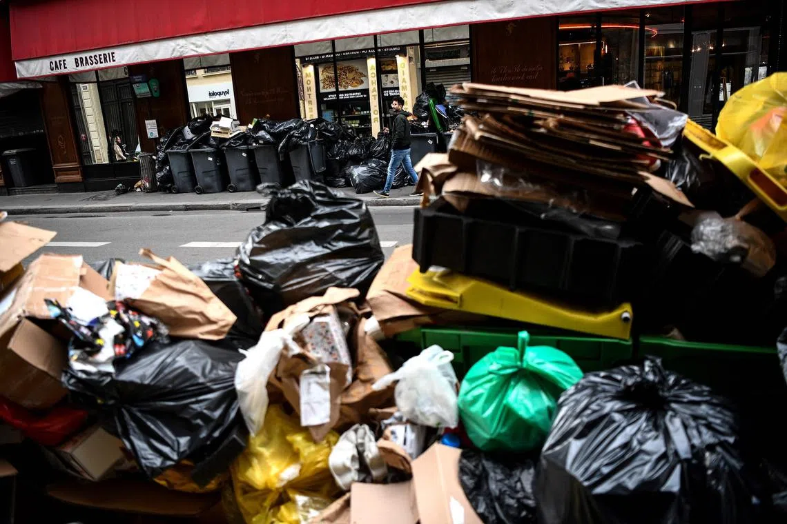 TOPSHOT - A man (top) walks past a pile of garbage bags that have been piling up since waste collectors went on strike against the French government's proposed pensions reform, outside a restaurant in Paris on March 15, 2023. - France faces another day of strikes on March 15, 2023, over highly contested pension reforms which President appears on the verge of pushing through despite months of protests. As the legislation enters the final stretch in parliament, trade unions are set to make another attempt to pressure the government and lawmakers into rejecting the proposed hike in the retirement age to 64. (Photo by Christophe ARCHAMBAULT / AFP)