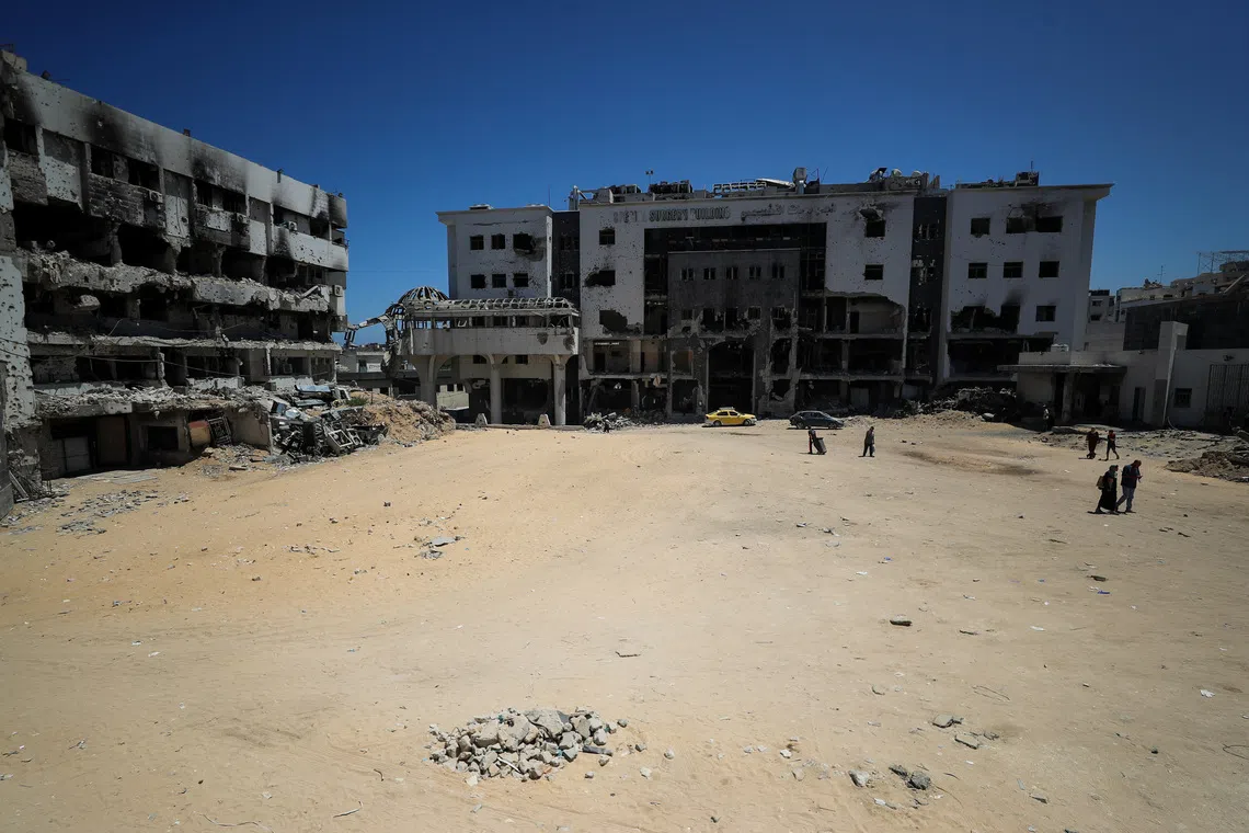 Palestinians walk next to a damaged building at Al-Shifa hospital in Gaza City, on July 9, 2025.