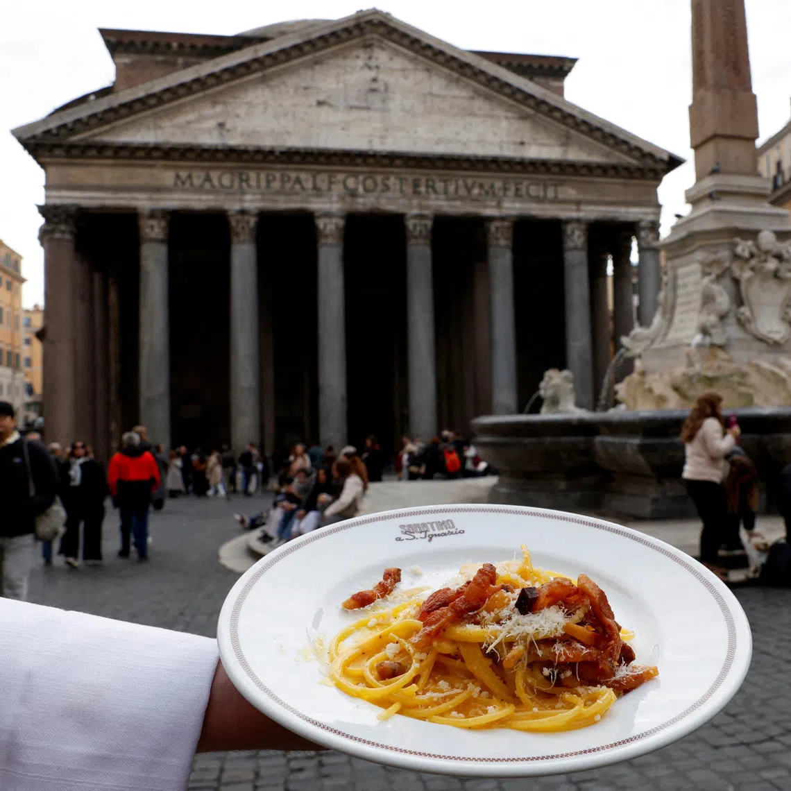 A waiter shows a plate of traditional pasta Carbonara in front of the Pantheon as Italian cuisine awaits a crucial UNESCO decision that could recognise it as an Intangible Cultural Heritage of Humanity in this illustration picture taken in Rome, Italy, December 3, 2025. REUTERS/Remo Casilli/ Illustration