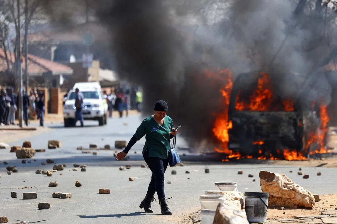 A local walking past a minibus taxi that was set on fire, following local reports of a killing of an e-hailing driver the previous day, amid ongoing violence between online ride-hailing operators and minibus taxi owners, outside Maponya Mall in Soweto, South Africa, Aug 14, 2025. 