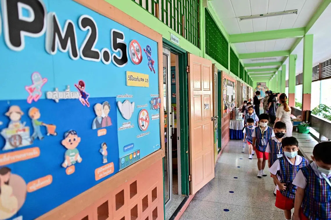 This photo taken on January 22, 2024 shows pupils wearing face masks walking past a poster about PM2.5 pollution particles at Suanlumpinee School in Bangkok. Hundreds of Thai children strain to sing the national anthem, reedy voices and fragile lungs competing against eight lanes of belching traffic next to their school's open atrium in central Bangkok. (Photo by MANAN VATSYAYANA / AFP) / To go with 'THAILAND-ENVIRONMENT-POLLUTION-EDUCATION,FOCUS' by Watsamon Tri-Yasakda and Rose Troup Buchanan