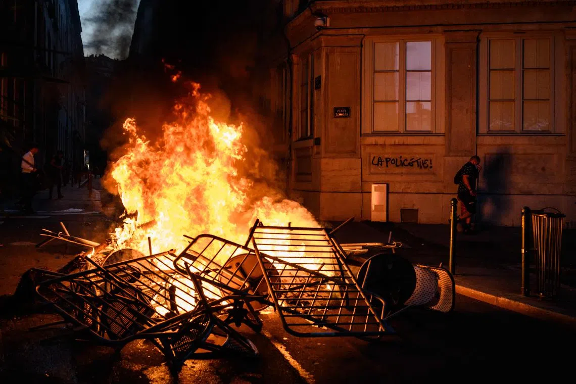 A woman walks past a wall lit up by a nearby fire on which is written, 'Police kill', during clashes with police.