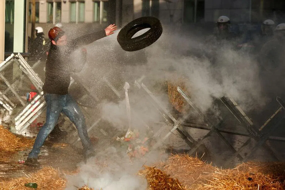 FILE PHOTO: A demonstrator throws a tyre over a barricade next to police officers in riot gear as he is sprayed with water amid smoke, during a protest by farmers from Belgium and other European countries near the European Parliament over price pressures, taxes and green regulation, on the day of an EU summit in Brussels, Belgium February 1, 2024. REUTERS/Yves Herman/File Photo