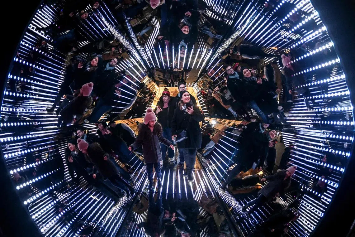 People standing in a giant kaleidoscope, an installation by French artist Guillaume Marmin, during the Festival of Lights, in Lyon, central eastern France, on Dec 7, 2023. 