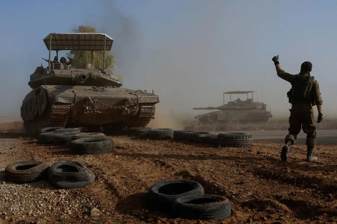An Israeli soldier gesturing towards a tank crew member as it crosses a road, as part of the convoy, amid the ongoing conflict between Israel and the Palestinian Islamist group Hamas, near Israel's border with southern Gaza, Dec 4, 2023. 