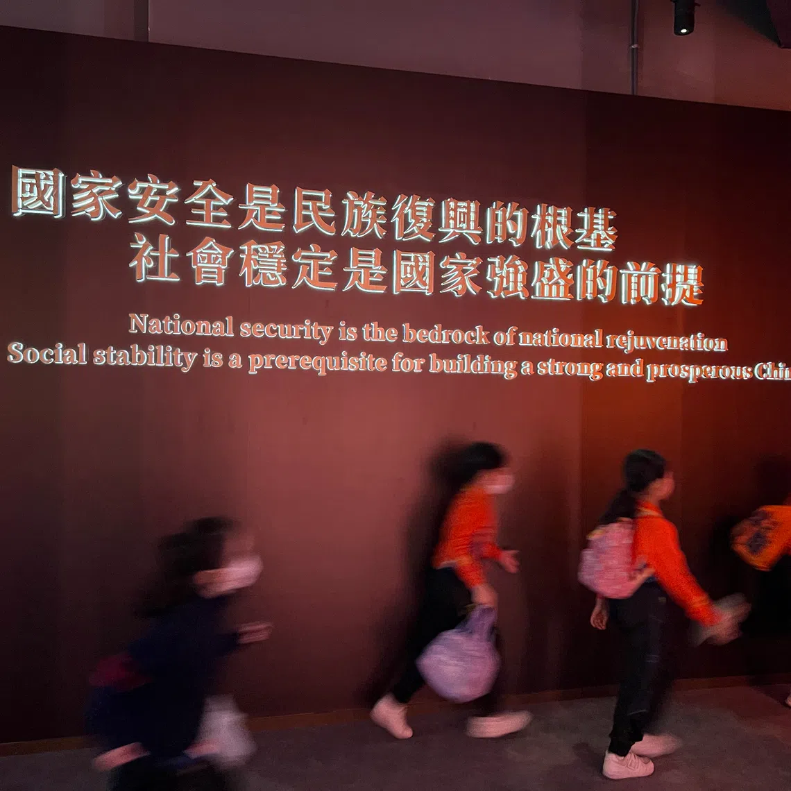 mfnational - Primary schoolers run past a board at the national security exhibition gallery in Hong Kong.