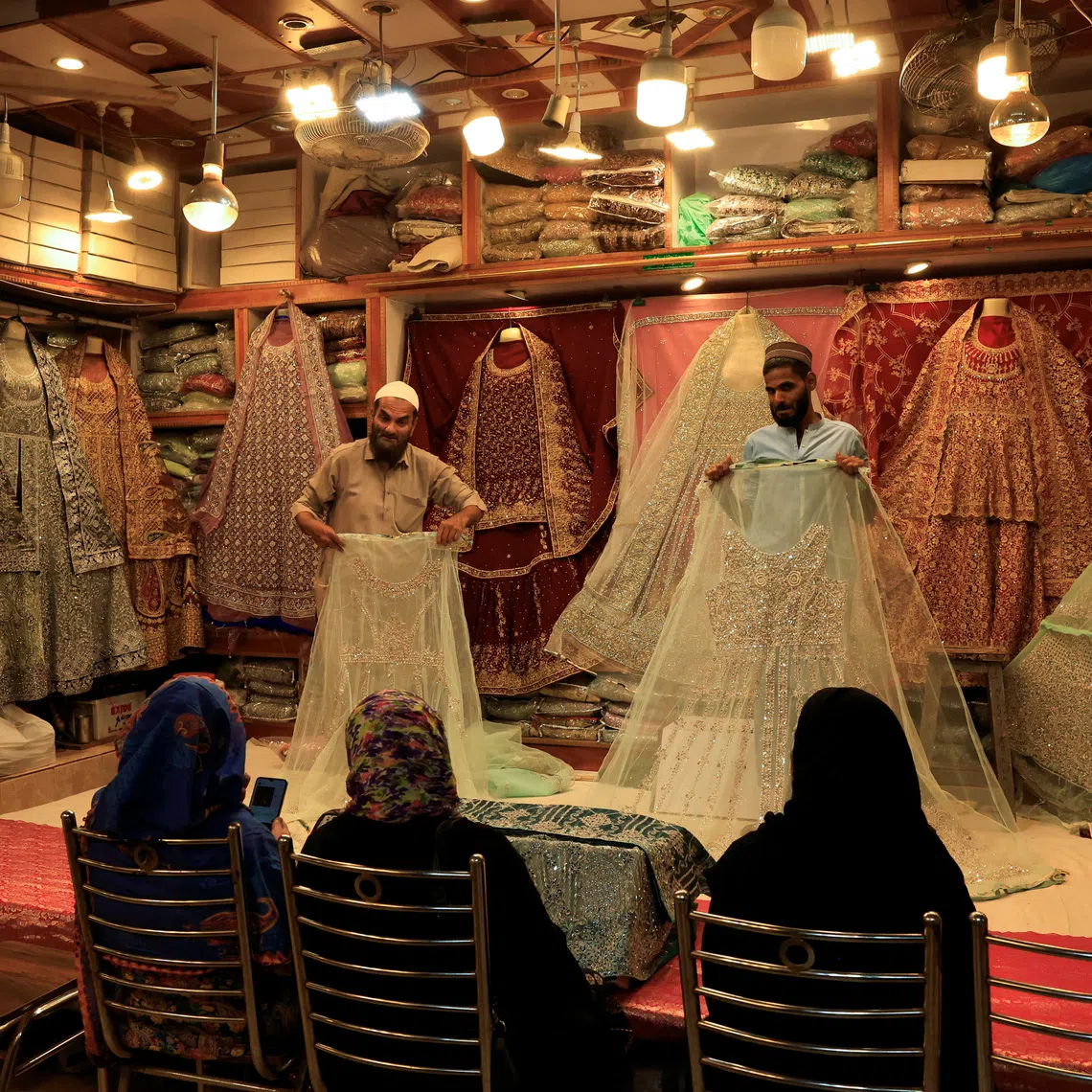 FILE PHOTO: Shopkeepers display bridal dresses to customers at a shop in a cloth market in Karachi, Pakistan September 23, 2025. REUTERS/Akhtar Soomro/File Photo