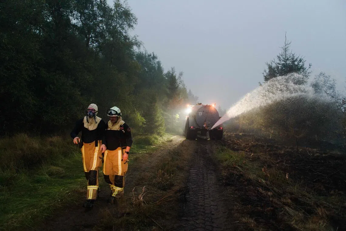 Firefighters walking along a road as farmers spray water with their tank to assist firefighters during operations against a wildfire at the Hautes Fagnes nature reserve near Sourbrodt, eastern Belgium, on Aug 17.