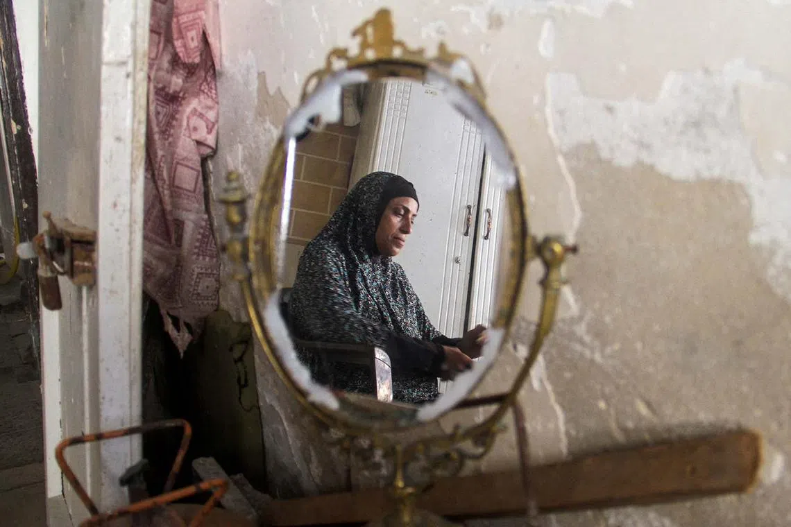 A Palestinian woman, Umm Al-Abd Ouda, is reflected in a mirror as she has lunch with her husband inside her house that was damaged in an Israeli strike, amid Israel-Hamas conflict, in Jabalia, in the northern Gaza Strip, Aug 26, 2024.