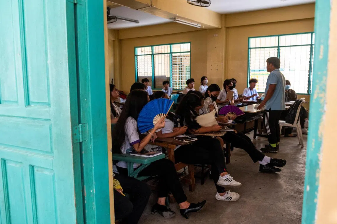 Grade 12 students use portable electric fans and hand fans as they attend a class at the Commonwealth High School, in Quezon City, Metro Manila, Philippines, April 18, 2024. REUTERS/Lisa Marie David