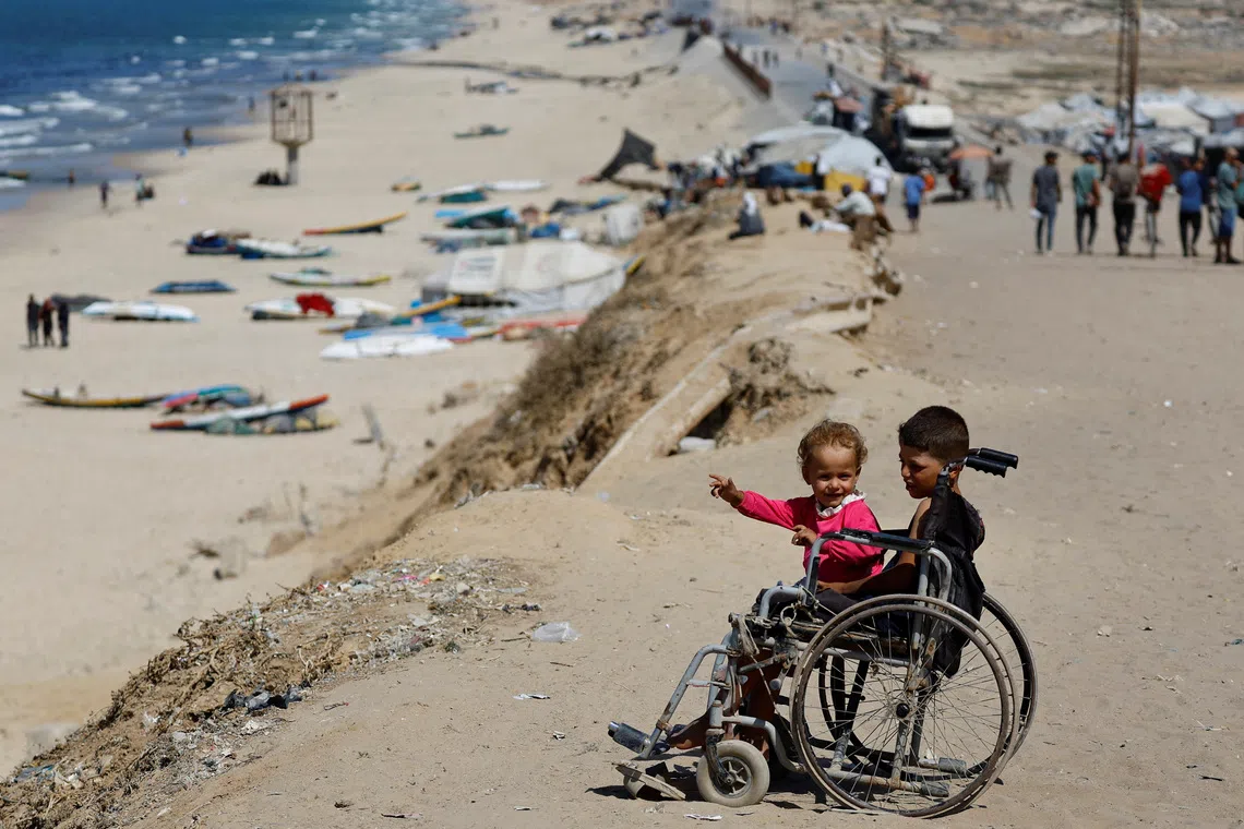 Displaced Palestinian children sit in a wheelchair by the side of a road, after Hamas agreed to release hostages and accept some other terms in a U.S. plan to end the war, in the central Gaza Strip, October 4, 2025. REUTERS/Mahmoud Issa