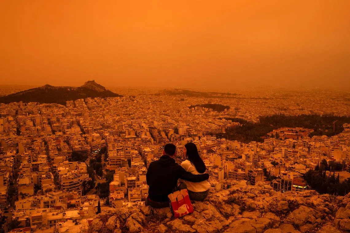 A couple sits on Tourkovounia hill, as southerly winds carry waves of Saharan dust, in Athens, on April 23, 2024. Clouds of dust blown in from the Sahara covered Athens and other Greek cities in one of the worst such episodes to hit the country since 2018. The yellow-orange haze smothered several regions, limiting visibility and prompting warnings of breathing risks from the authorities. 