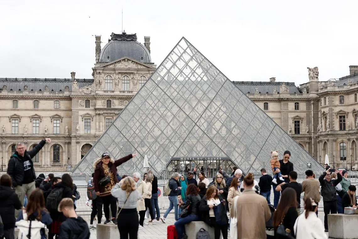 People stand near the glass Pyramid of the Louvre Museum as the museum remains closed the day after a spectacular jewel heist.