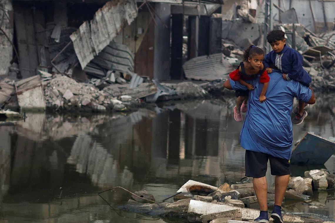 FILE PHOTO: A Palestinian man holds his children as he walks next to buildings destroyed in an Israeli strike, amid the ongoing conflict between Israel and Hamas, in Khan Younis, in the southern Gaza Strip, June 30, 2024. REUTERS/Mohammed Salem/File Photo