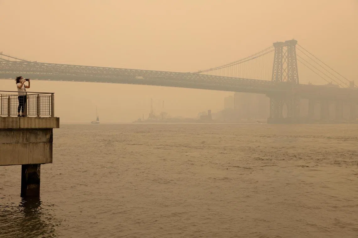 A person wearing a face mask takes a picture of the Manhattan skyline while it is covered in haze and smoke caused by wildfires in Canada, in Brooklyn on Wednesday. 