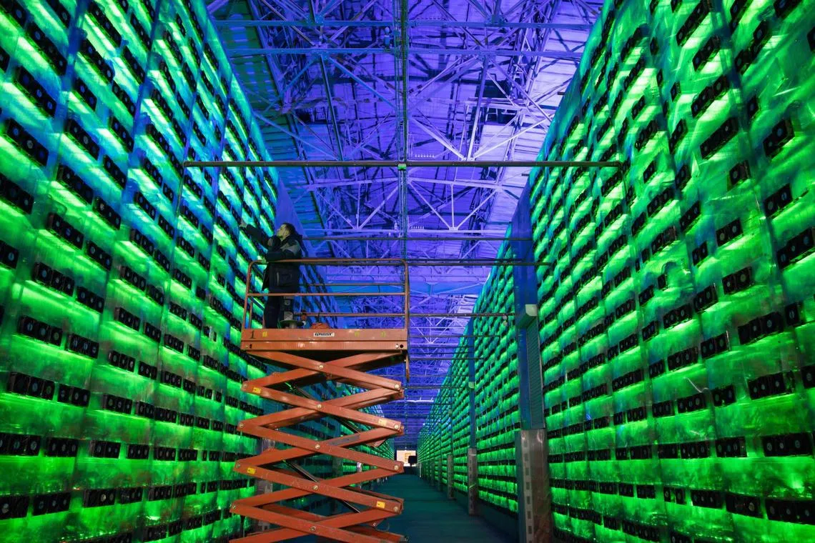 A technician on a cherry picker inspects racks of illuminated mining rigs at a cryptocurrency mining centre in Nadvoitsy, Russia.