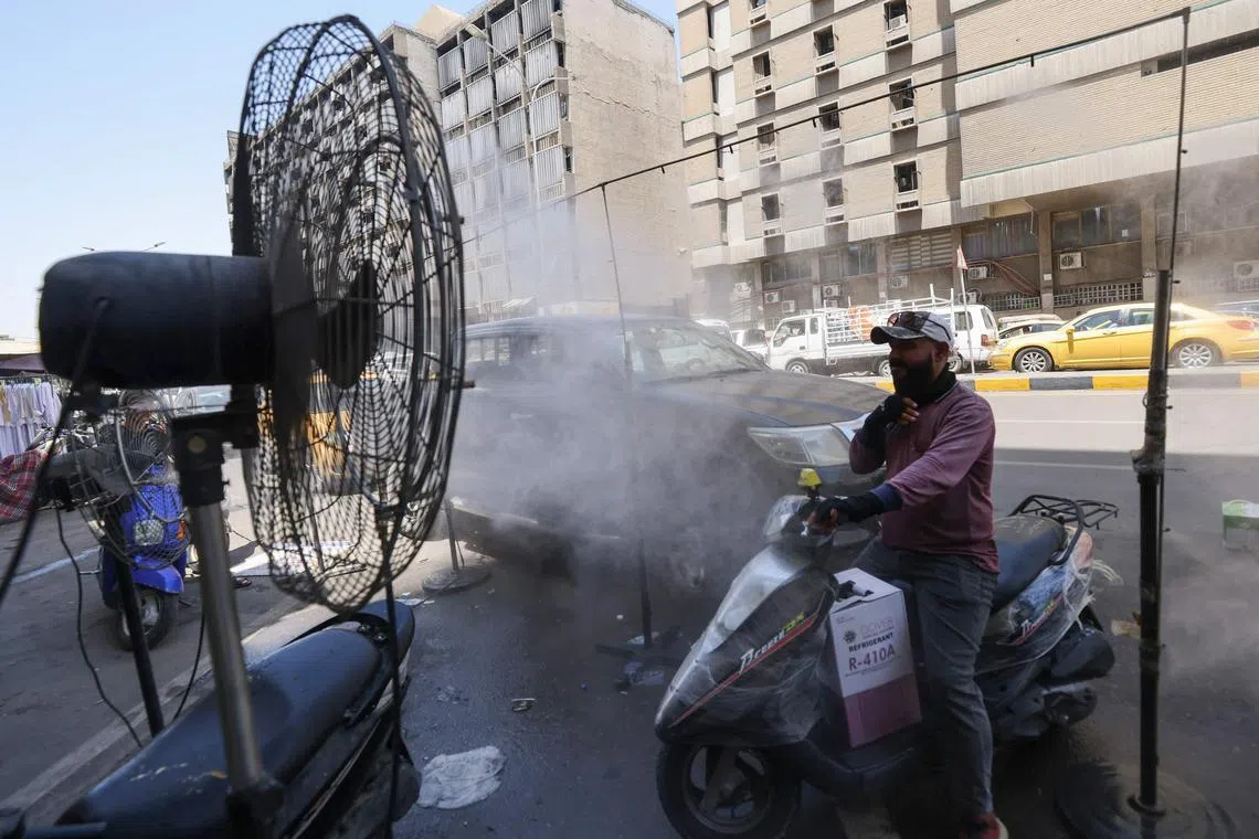A man cools off with a mist dispenser set up on a street in central Baghdad, amid soaring temperatures.