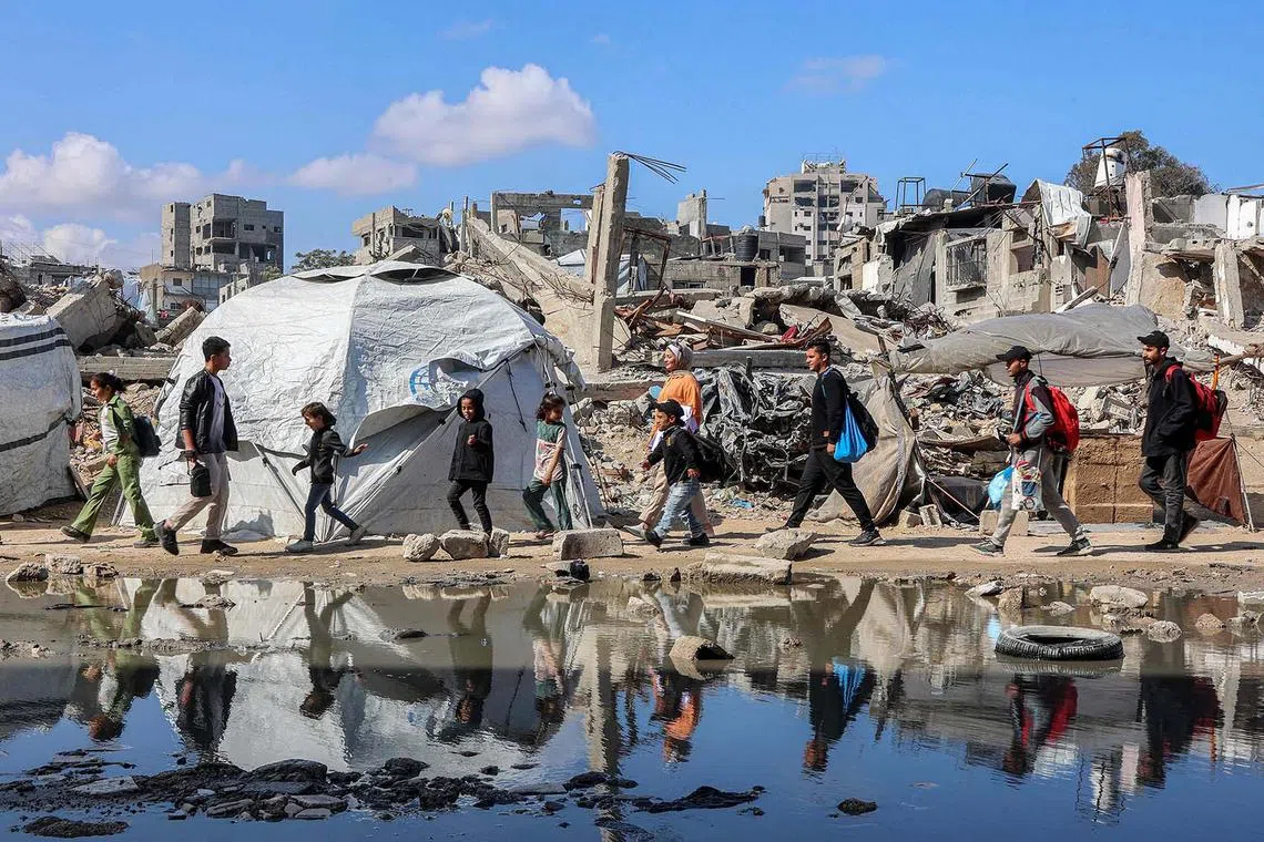 TOPSHOT - People walk past a puddle of water by a tent shelter erected near the rubble of a collapsed building in the Nasr neighbourhood in western Gaza City on April 15, 2025. Israel said on April 12 that it planned to expand its military offensive in Gaza after seizing a new corridor as part of a broader effort to take large parts of the war-battered Palestinian territory. The previous truce with the Palestinian Hamas movement brokered by the US, Egypt, and Qatar which took effect on January 19 collapsed on March 18 as Israel resumed intense strikes on Gaza. (Photo by Omar AL-QATTAA / AFP)