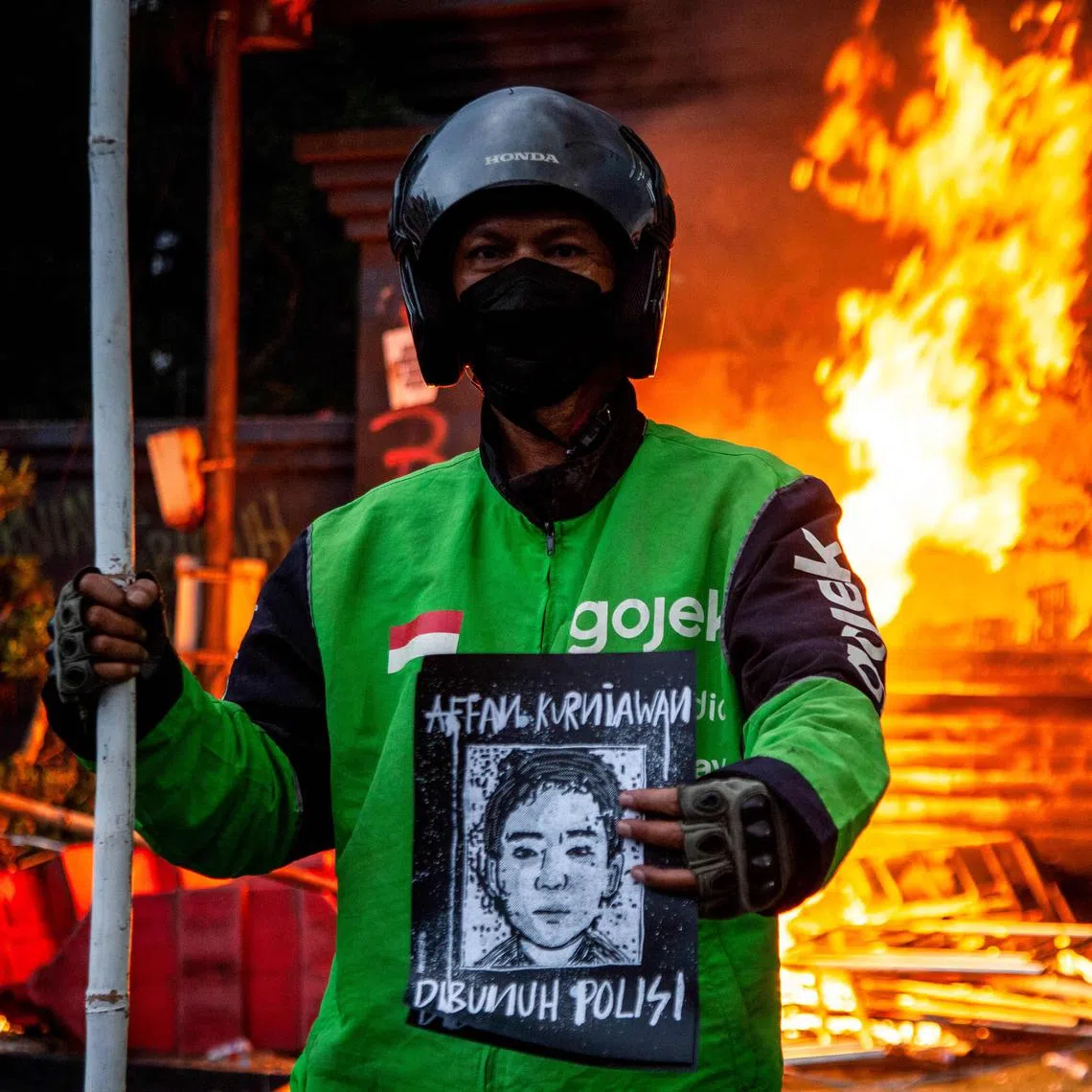 A man wearing a biker's jacket holds a portrait of the motorcycle taxi driver who was run over by an armoured Brimob (Mobile Brigade Corps) vehicle the night before, during a protest against police in front of the Greater Jakarta Metropolitan Regional Police headquarters in Jakarta on August 29, 2025. Protests erupted across several Indonesian cities on August 29 in anger at the death of a motorcycle taxi driver hit by a police vehicle, as officers responded with tear gas and the president called for calm. (Photo by Aditya IRAWAN / AFP)
