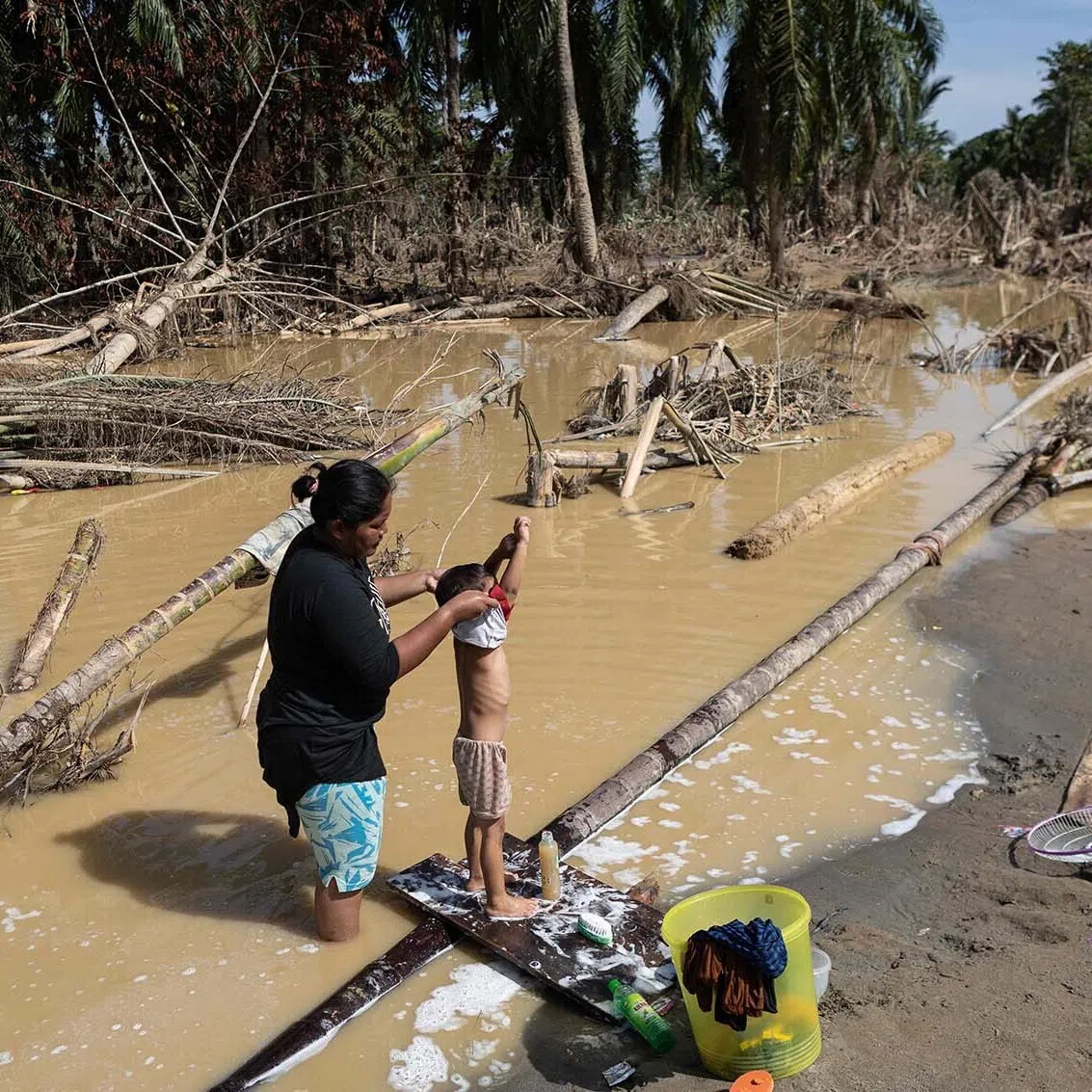 A mother bathing her child in muddy waters amid a clean water shortage in the aftermath of flash floods at Aceh Tamiang in Northern Sumatra on Dec 10, 2025.