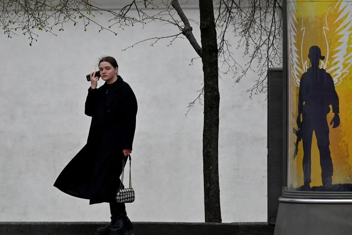 A pedestrian takes a phone call near a placard reading "The Armed Forces of Ukraine are our guardian angels" in Kyiv on April 9, 2026, amid Russian invasion in Ukraine. (Photo by Sergei SUPINSKY / AFP)