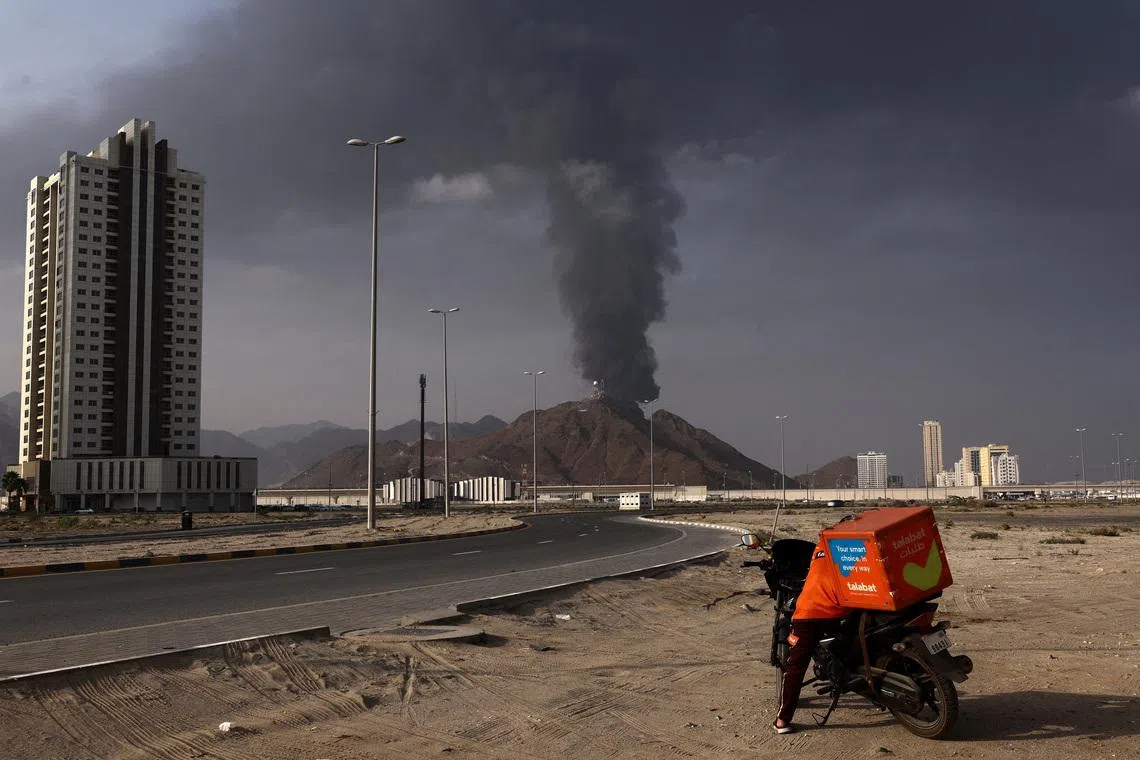 A person stands next to a motorcycle as smoke rises in the Fujairah oil industry zone following a fire caused by debris after interception of a drone by air defenses, according to the Fujairah media office, amid the U.S.-Israel conflict with Iran, in Fujairah, United Arab Emirates, March 3, 2026. REUTERS/Amr Alfiky