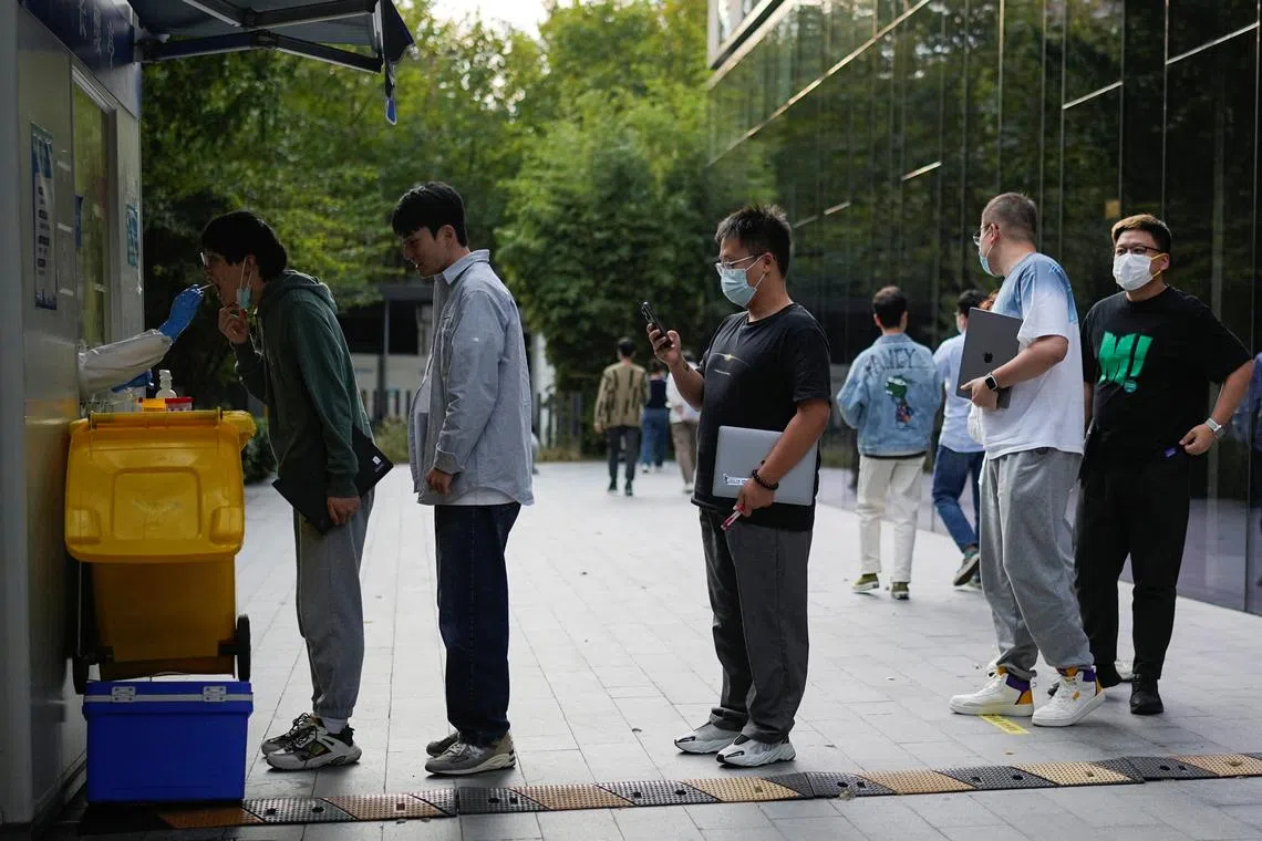 People holding laptops line up to get tested for the coronavirus disease (Covid-19) at a nucleic acid testing site at an office building, following the coronavirus disease (Covid-19) outbreak in Shanghai, China, November 3, 2022. 