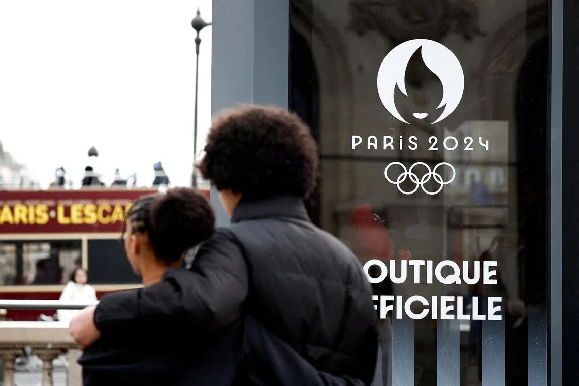 People walk near the logo of the Paris 2024 Olympic and Paralympic Games on an official Paris 2024 store at Place de l'Opera in Paris.
