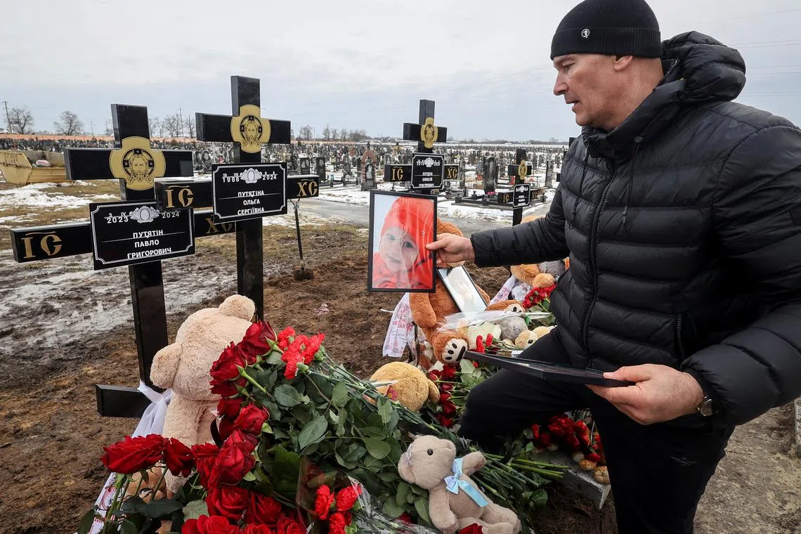 A man places a portrait on a grave during a funeral ceremony for a family of two adults and three children, local residents who were killed on Friday, February 9, at their house that burned in a Russian drone strike, amid Russia's attack on Ukraine, in Kharkiv, Ukraine February 12, 2024. REUTERS/Vyacheslav Madiyevskyy/ File Photo