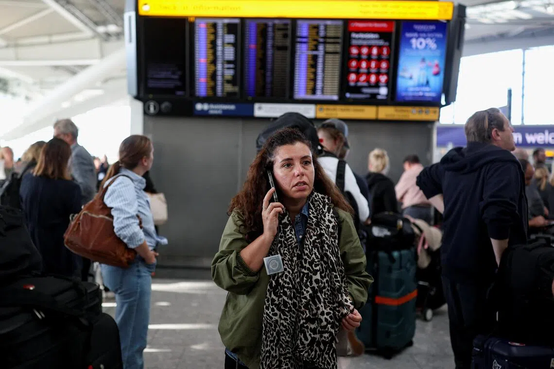 A passenger uses a mobile phone while others look at a departure board displaying cancelled flights at Heathrow Airport’s Terminal 5 in London, Britain, on Sept 8.