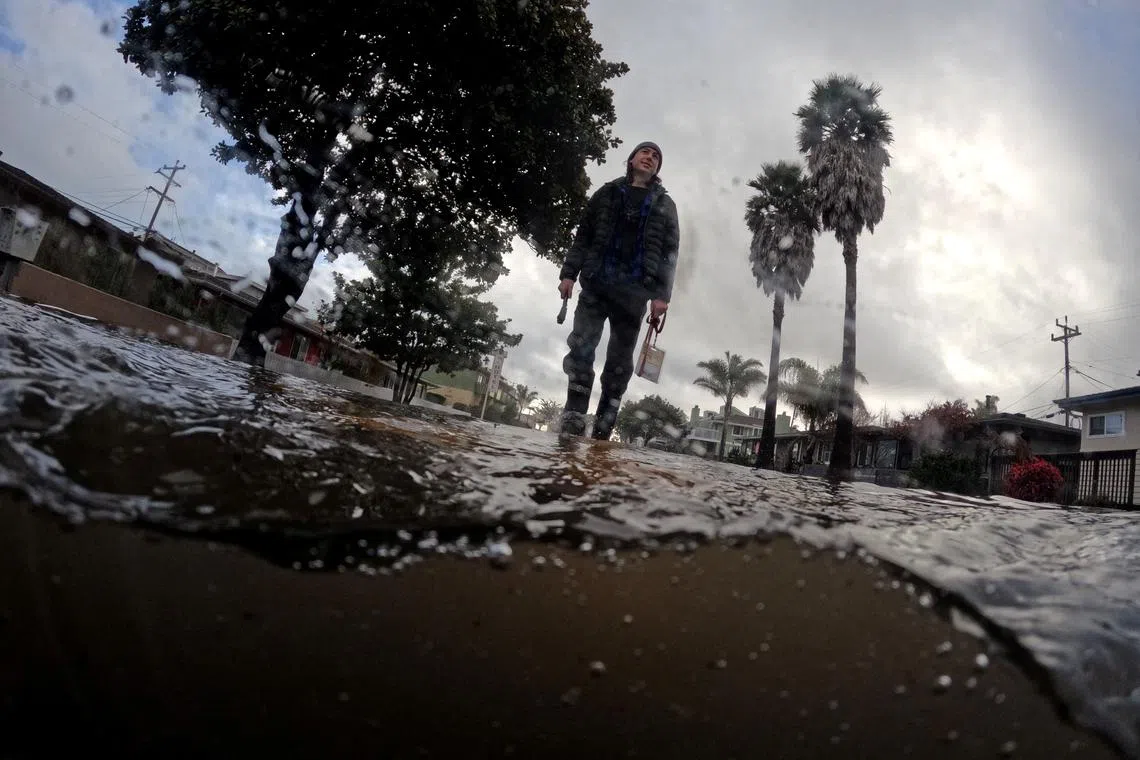 A resident walks along a flooded street in the coastal town of Aptos, U.S., Jan 5, 2023.