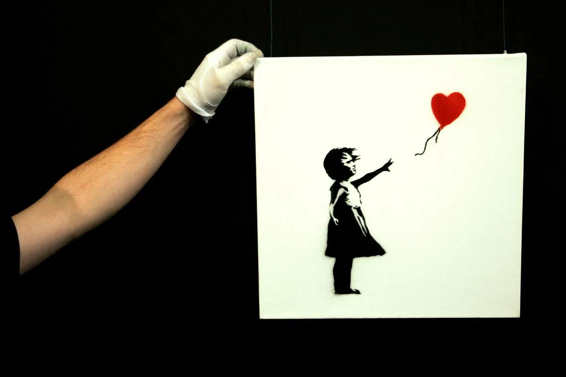 FILE PHOTO: A gallery technician adjusts Banksy's artwork \"Balloon Girl\" (1975) at Sotheby's auction house at Olympia in London February 2, 2007. REUTERS / Luke MacGregor (BRITAIN)/File Photo