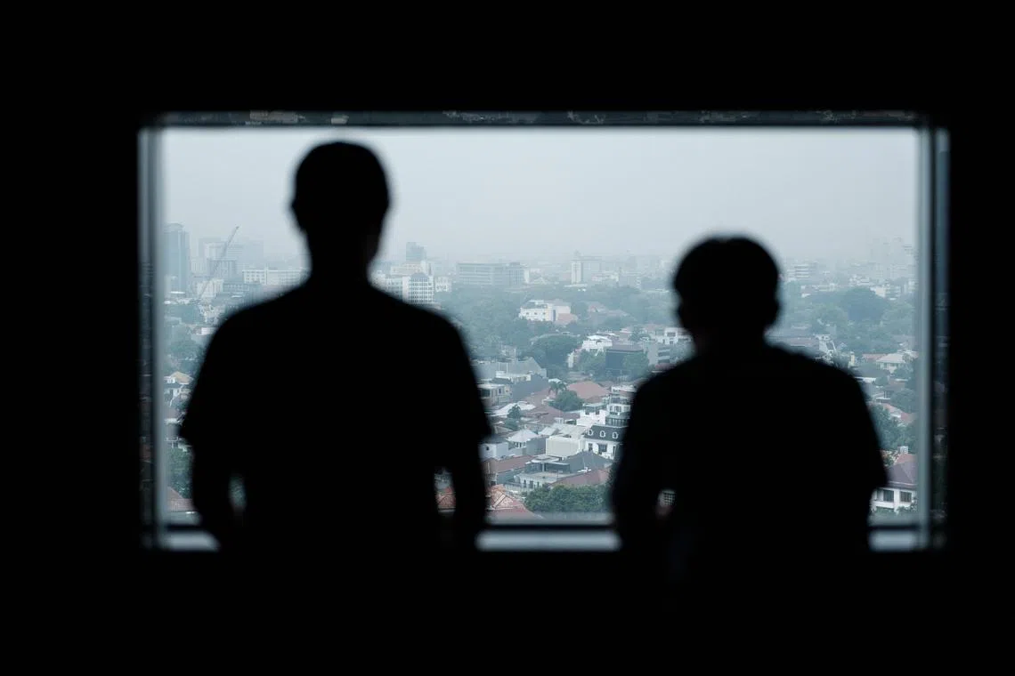 Two Indonesians who were forced to work at a scam farm in Cambodia ook out of a window at a shelter in Jakarta.