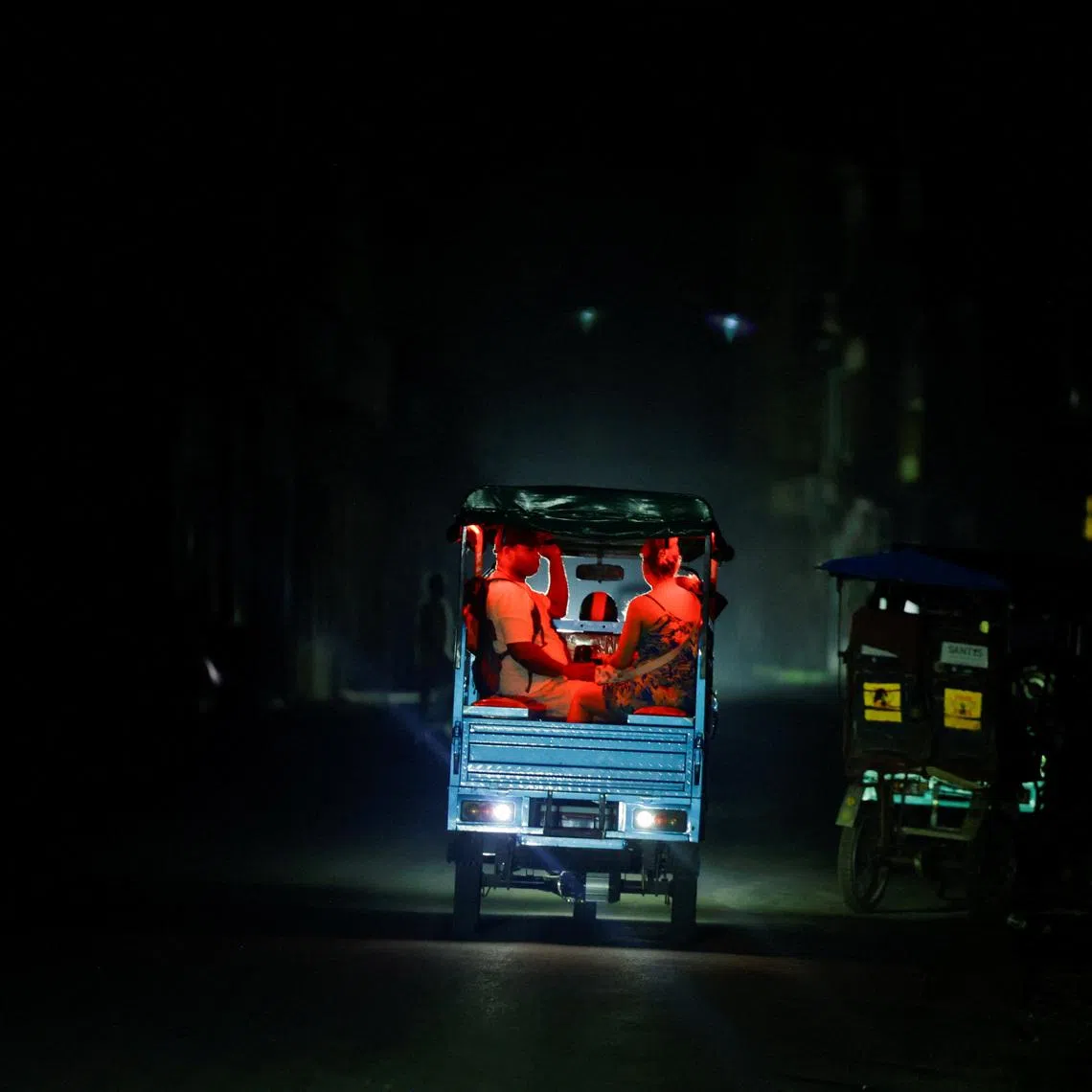 People ride an electric tricycle, one of the few modes of transportation still functioning, as Cuba's national power grid collapsed, marking the third major outage in nine days, in Havana, Cuba, July 14, 2026. REUTERS/Norlys Perez