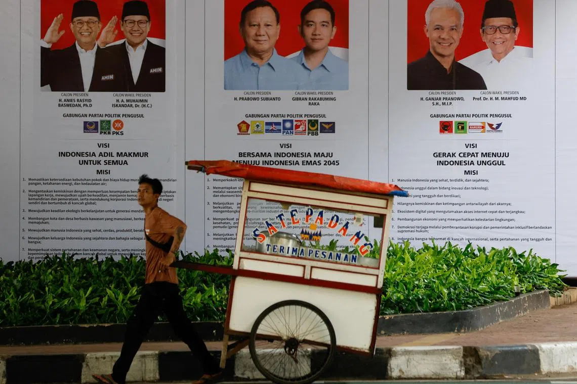 A street vendor pulls his cart past a banner showing presidential candidates contesting the upcoming general election in Jakarta, Indonesia, January 12, 2024. REUTERS/Willy Kurniawan